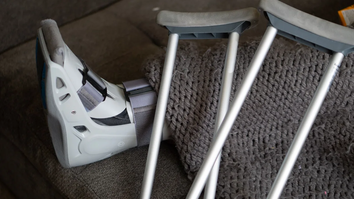 Bota ortopédica e par de muletas apoiadas no sofá durante a recuperação